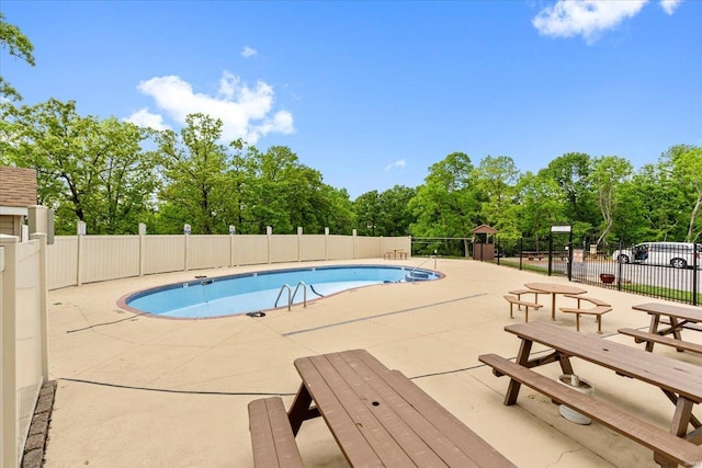 community pool featuring fence, a patio, and view of wooded area