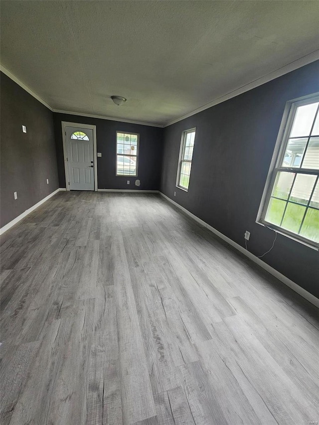 unfurnished living room with wood finished floors, baseboards, ornamental molding, and a textured ceiling