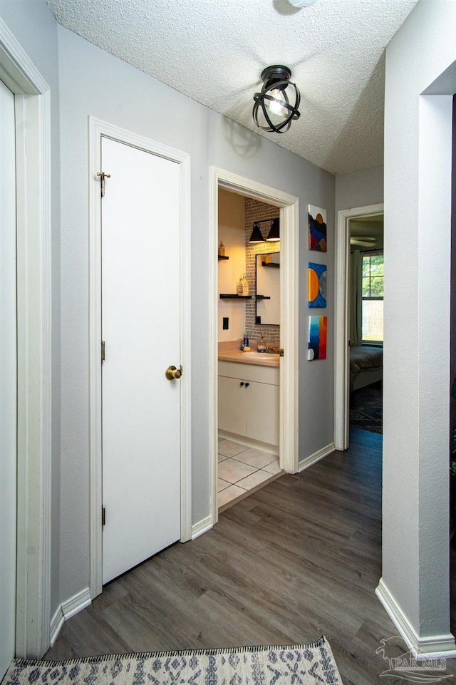 hallway with a textured ceiling, sink, and dark wood-type flooring