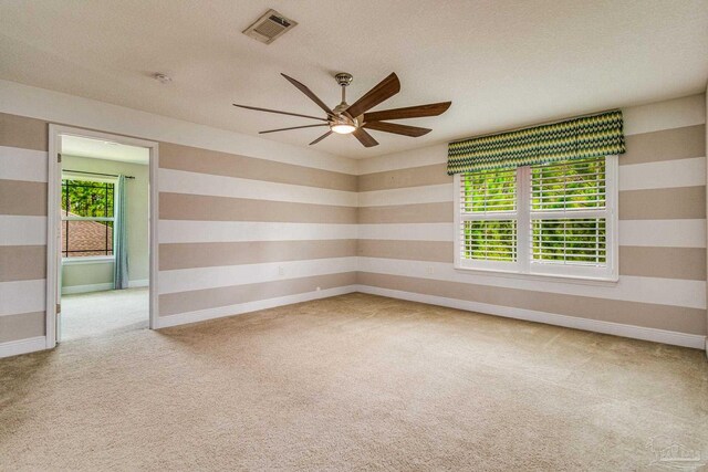 empty room with a textured ceiling, ceiling fan, a wealth of natural light, and light colored carpet