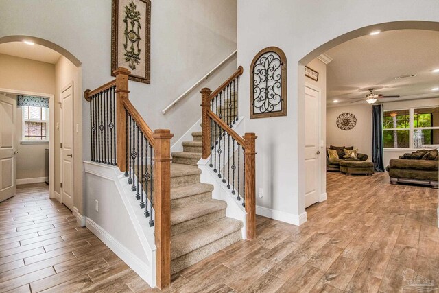 stairway featuring a high ceiling, light hardwood / wood-style flooring, and ceiling fan