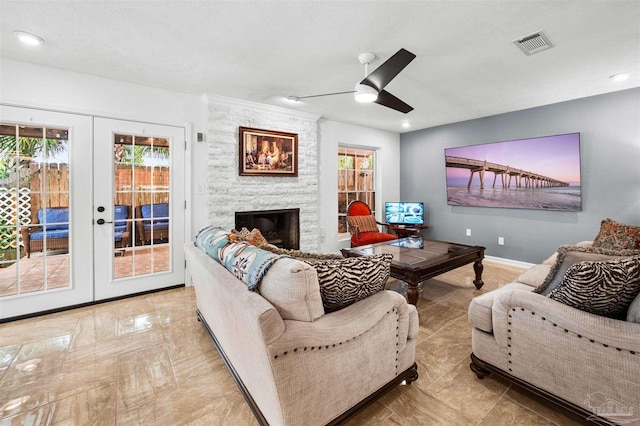 living room with ceiling fan, a stone fireplace, french doors, and a textured ceiling