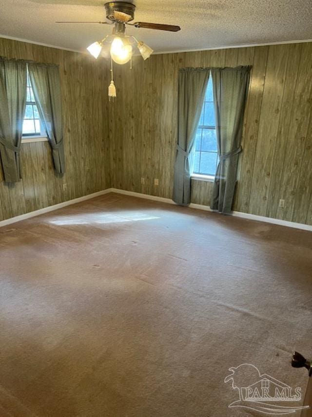 carpeted spare room featuring ceiling fan, a healthy amount of sunlight, wooden walls, and a textured ceiling