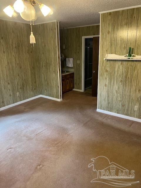 unfurnished living room with crown molding, wood walls, a textured ceiling, and carpet flooring