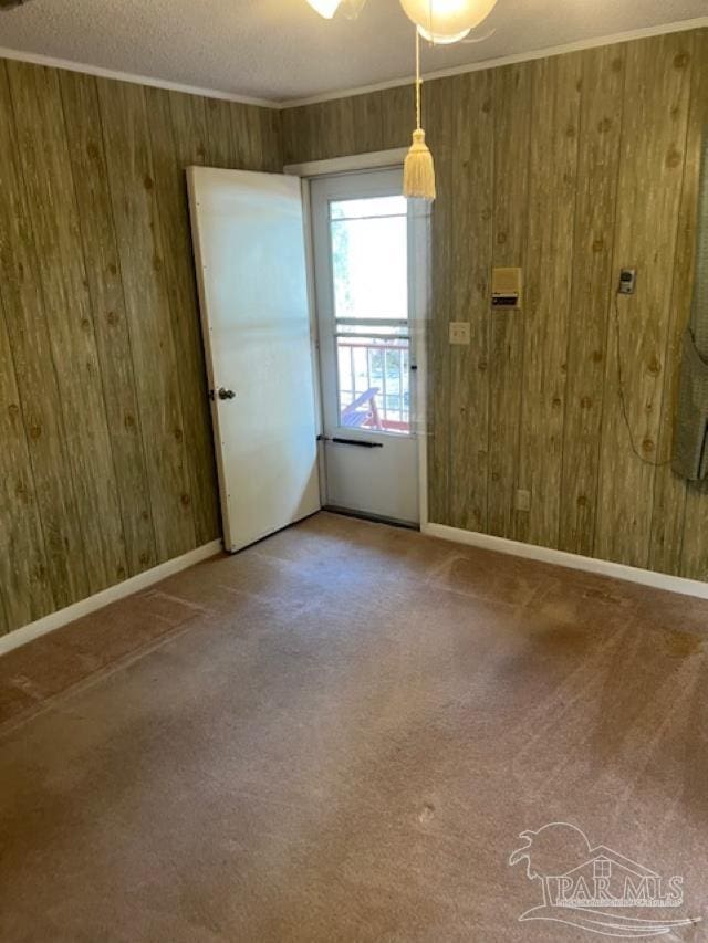 spare room with crown molding, wooden walls, and carpet