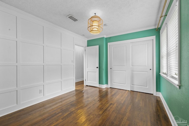 unfurnished bedroom featuring ornamental molding, a textured ceiling, dark hardwood / wood-style flooring, and multiple windows