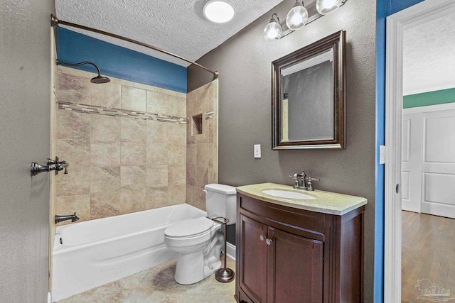 full bathroom featuring a textured ceiling, vanity, toilet, and tiled shower / bath