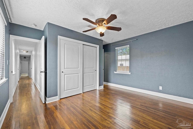 unfurnished bedroom featuring ceiling fan, a textured ceiling, a closet, and dark hardwood / wood-style flooring