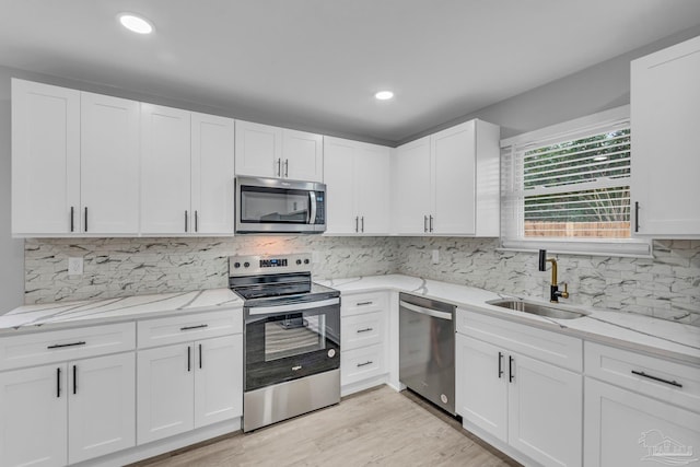 kitchen with light stone counters, a sink, white cabinets, appliances with stainless steel finishes, and light wood finished floors