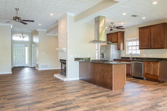 kitchen with appliances with stainless steel finishes, dark hardwood / wood-style floors, island range hood, ornamental molding, and kitchen peninsula