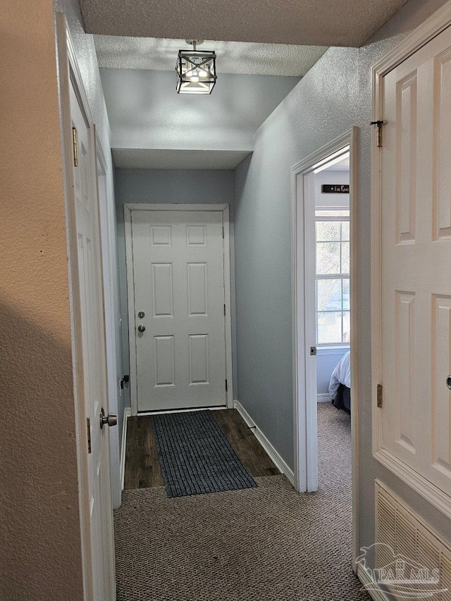 doorway to outside featuring a textured ceiling and dark carpet