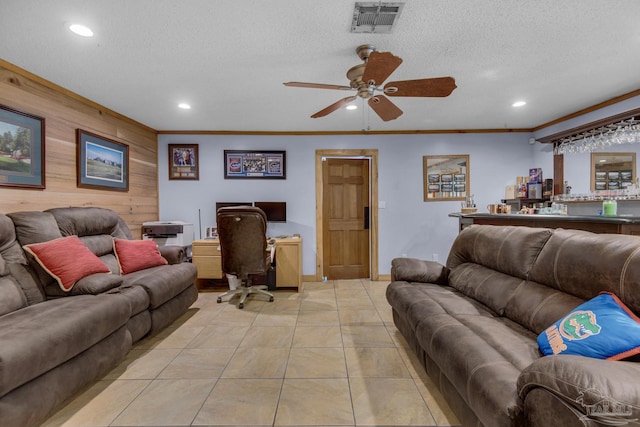 living room with light tile patterned floors, wooden walls, ornamental molding, and a textured ceiling