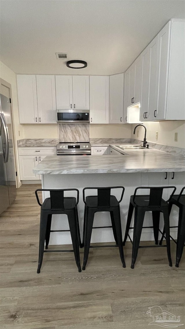 kitchen with a breakfast bar, white cabinets, kitchen peninsula, and appliances with stainless steel finishes