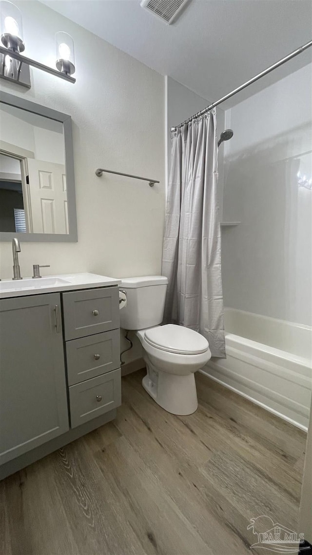 full bathroom featuring toilet, shower / bathtub combination with curtain, hardwood / wood-style floors, and vanity