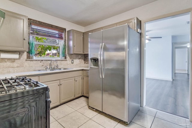 kitchen featuring tasteful backsplash, sink, light tile patterned flooring, black gas range oven, and stainless steel fridge