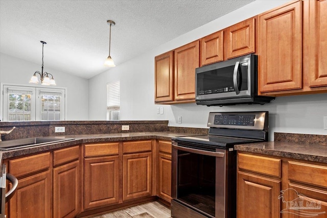 kitchen with pendant lighting, sink, stainless steel appliances, a textured ceiling, and vaulted ceiling