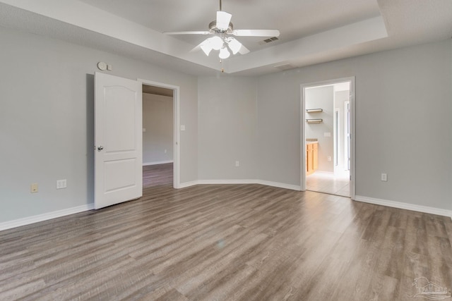 unfurnished bedroom with a raised ceiling, wood finished floors, visible vents, and baseboards