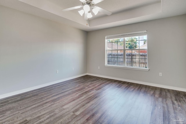 unfurnished room with dark wood-type flooring, a ceiling fan, baseboards, and a raised ceiling