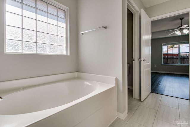 bathroom with baseboards, a bath, and a ceiling fan