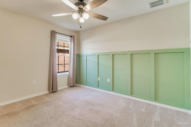 empty room with visible vents, a decorative wall, a ceiling fan, and carpet floors