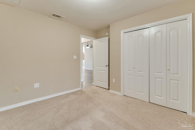 unfurnished bedroom featuring baseboards, visible vents, a closet, a textured ceiling, and light colored carpet