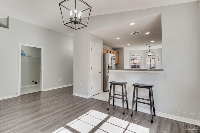 kitchen with a breakfast bar area, visible vents, stainless steel fridge with ice dispenser, light wood-style floors, and a chandelier