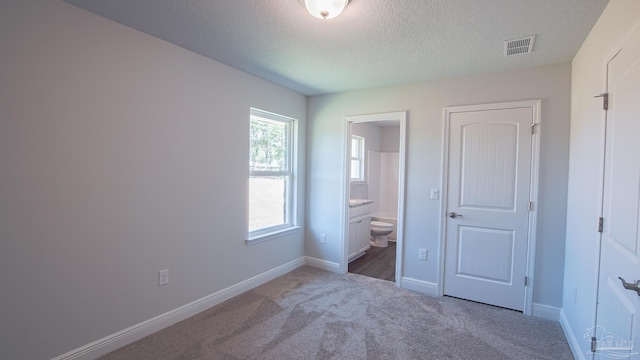 unfurnished bedroom featuring ensuite bath, carpet, and a textured ceiling