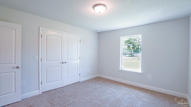 unfurnished bedroom with light colored carpet, a textured ceiling, and a closet