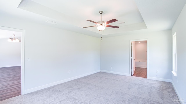 carpeted spare room with a tray ceiling and ceiling fan with notable chandelier