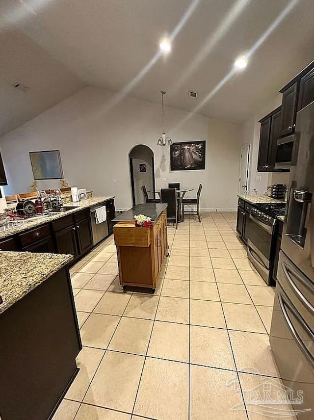 kitchen with a kitchen island, vaulted ceiling, light stone counters, stainless steel gas range, and light tile patterned floors