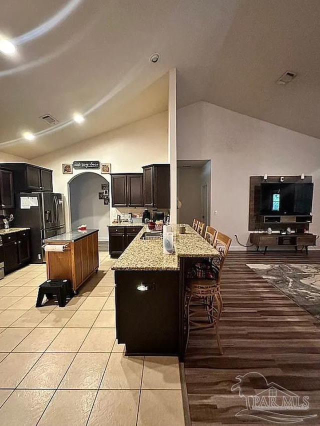 kitchen with a center island, light stone counters, stainless steel refrigerator with ice dispenser, a kitchen bar, and light tile patterned floors