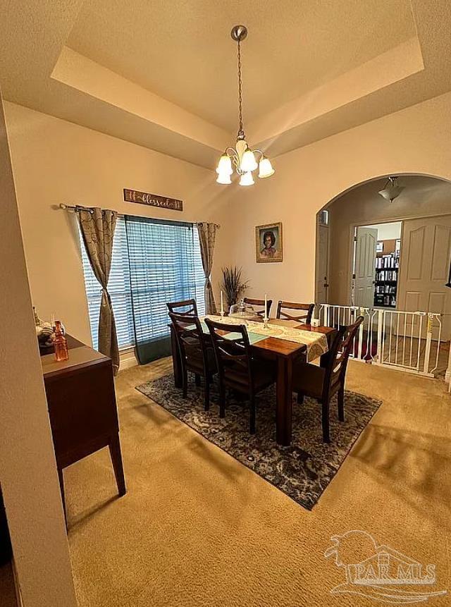 dining area featuring a notable chandelier, a tray ceiling, and carpet flooring