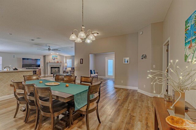 dining room featuring ceiling fan with notable chandelier, light hardwood / wood-style floors, and a tiled fireplace