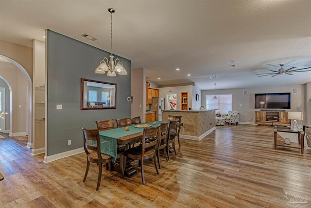 dining area with ceiling fan with notable chandelier and light wood-type flooring