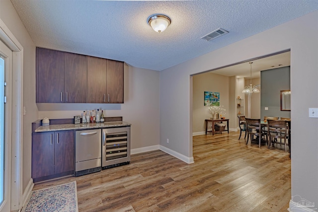 bar featuring dark brown cabinets, light hardwood / wood-style flooring, wine cooler, and stainless steel dishwasher