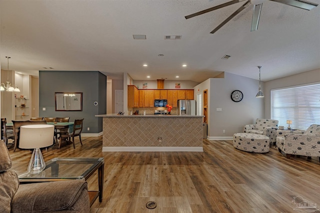 kitchen featuring light wood-type flooring, ceiling fan with notable chandelier, pendant lighting, stainless steel fridge with ice dispenser, and lofted ceiling