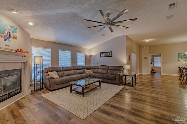 living room with a textured ceiling, a healthy amount of sunlight, a tile fireplace, hardwood / wood-style flooring, and lofted ceiling