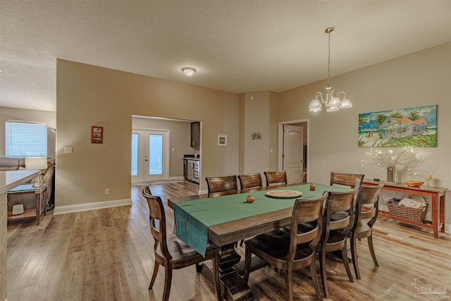 dining area featuring a textured ceiling, light wood-type flooring, french doors, and a chandelier