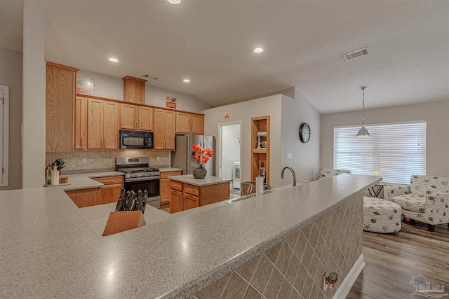 kitchen with lofted ceiling, hanging light fixtures, hardwood / wood-style flooring, appliances with stainless steel finishes, and tasteful backsplash