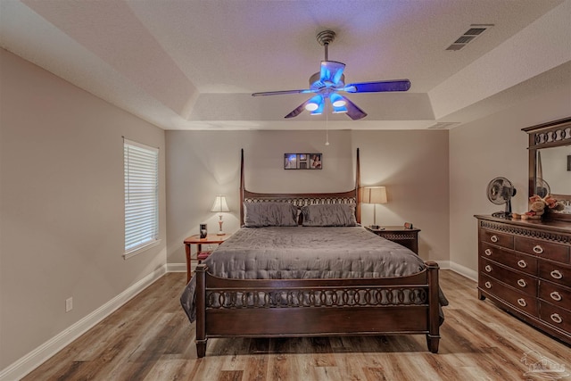 bedroom featuring hardwood / wood-style floors, ceiling fan, a textured ceiling, and a tray ceiling