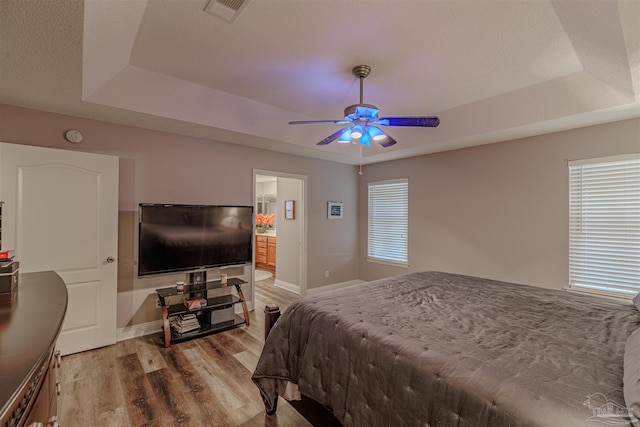 bedroom with a raised ceiling, ensuite bath, ceiling fan, and hardwood / wood-style floors