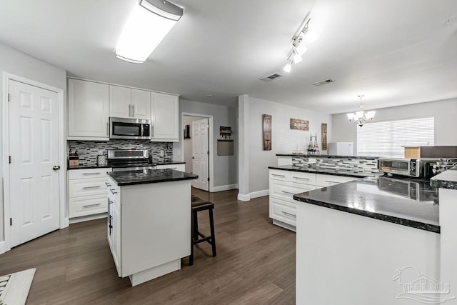 kitchen featuring dark hardwood / wood-style floors, stainless steel appliances, a center island, pendant lighting, and white cabinetry