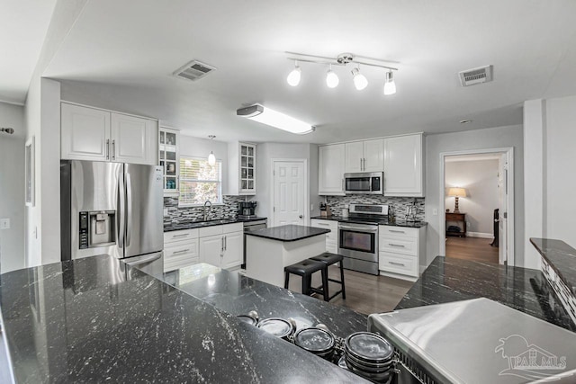 kitchen with white cabinets, tasteful backsplash, dark stone counters, stainless steel appliances, and a center island