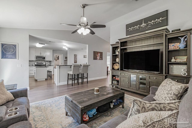 living room with light hardwood / wood-style flooring, ceiling fan, and vaulted ceiling