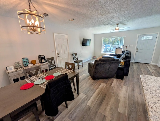 dining room with ceiling fan with notable chandelier, light wood-type flooring, and a textured ceiling