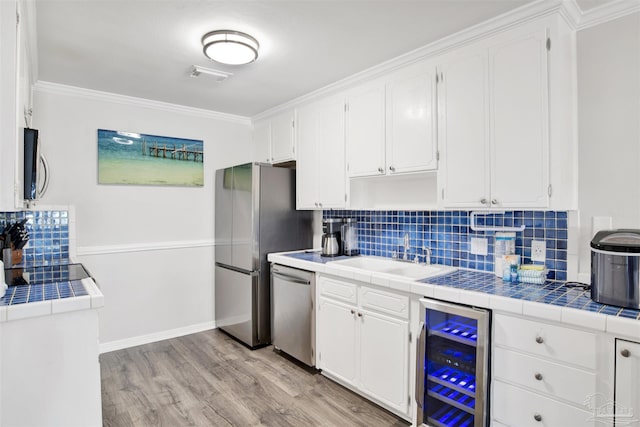 kitchen with appliances with stainless steel finishes, tile countertops, wine cooler, and sink