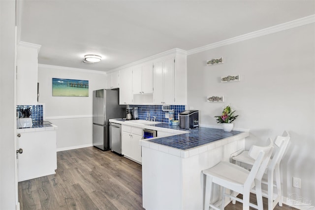 kitchen featuring white cabinetry, tile counters, stainless steel appliances, backsplash, and kitchen peninsula