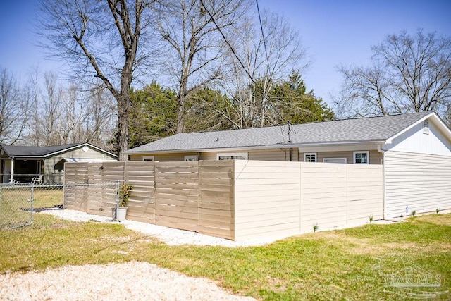 view of home's exterior with a shingled roof, a yard, and fence