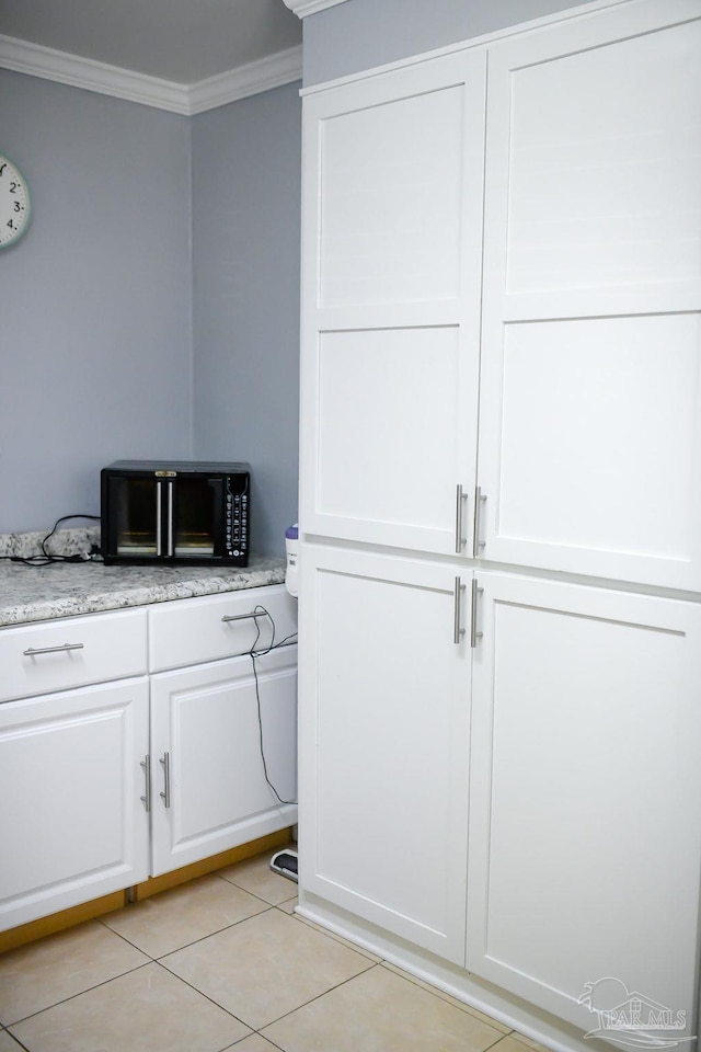 interior space featuring black microwave, light stone countertops, ornamental molding, light tile patterned floors, and white cabinets