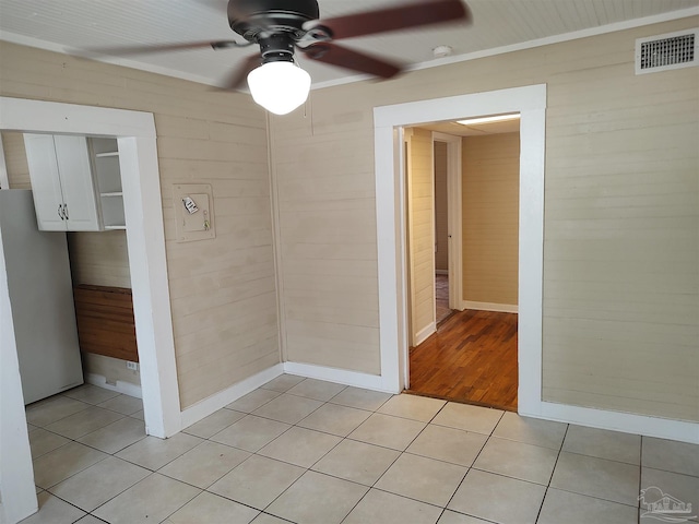 tiled spare room featuring ceiling fan and wood walls